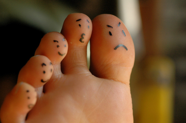 The ball of a foot and five toes with different emotions like a sad, worried, or happy face drawn on in pen; background blurred