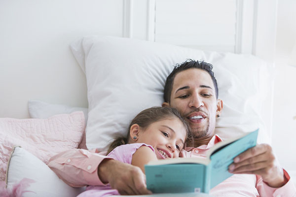photo of a father reading to his daughter as they snuggle in bed